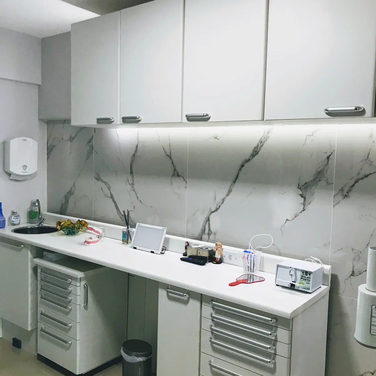 Consultório do Espaço Elias Affonso: bancada clara com armários brancos e parede de mármore