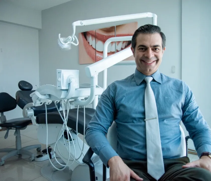 Dr. Glauco de Assis Affonso sentado no consultório, de camisa azul e gravata